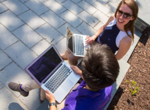 Two women with laptops talking on a park bench